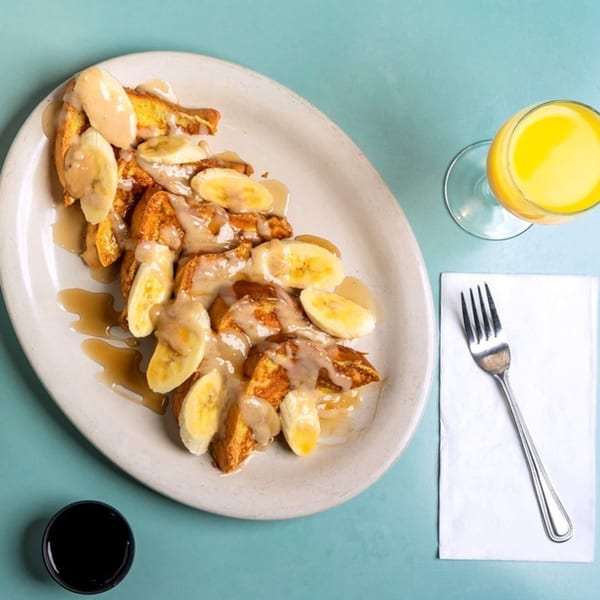 Banana French Toast with syrup and a side of orange juice and a fork on a blue table.