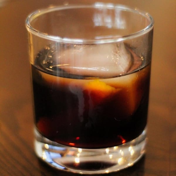 Dark beverage with a large ice cube in a clear glass on a wooden table.