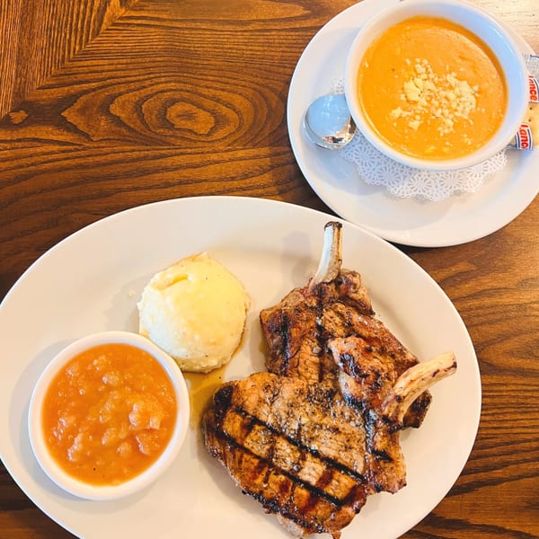 Grilled pork chops with mashed potatoes, applesauce, and a side of tomato soup with crackers.